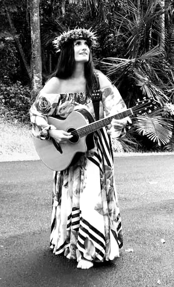 Stef Mariani in a haku lei playing acoustic guitar, black and white portrait